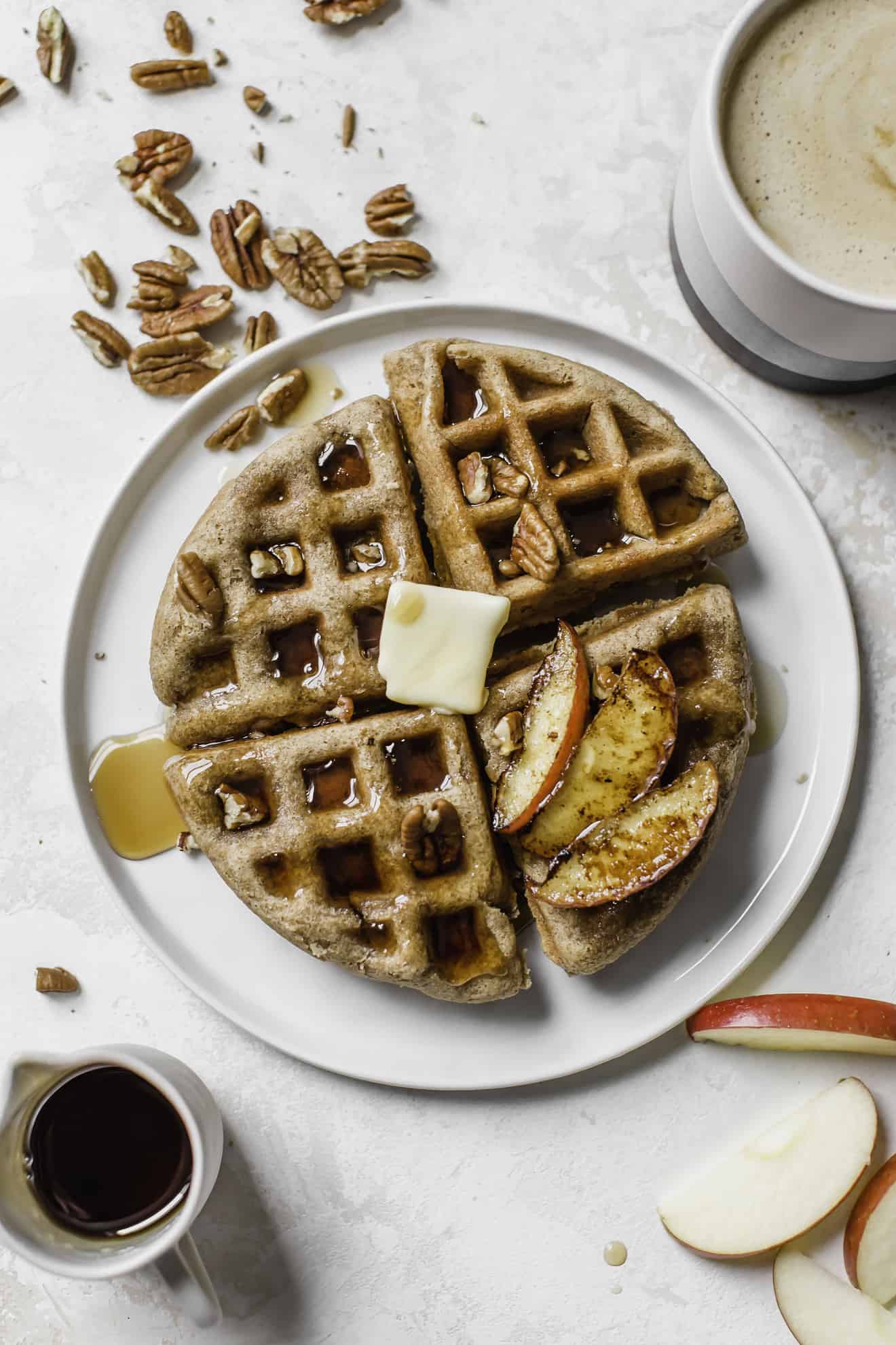 overhead image of pumpkin spice waffle on white plate with butter, maple syrup, and pecans