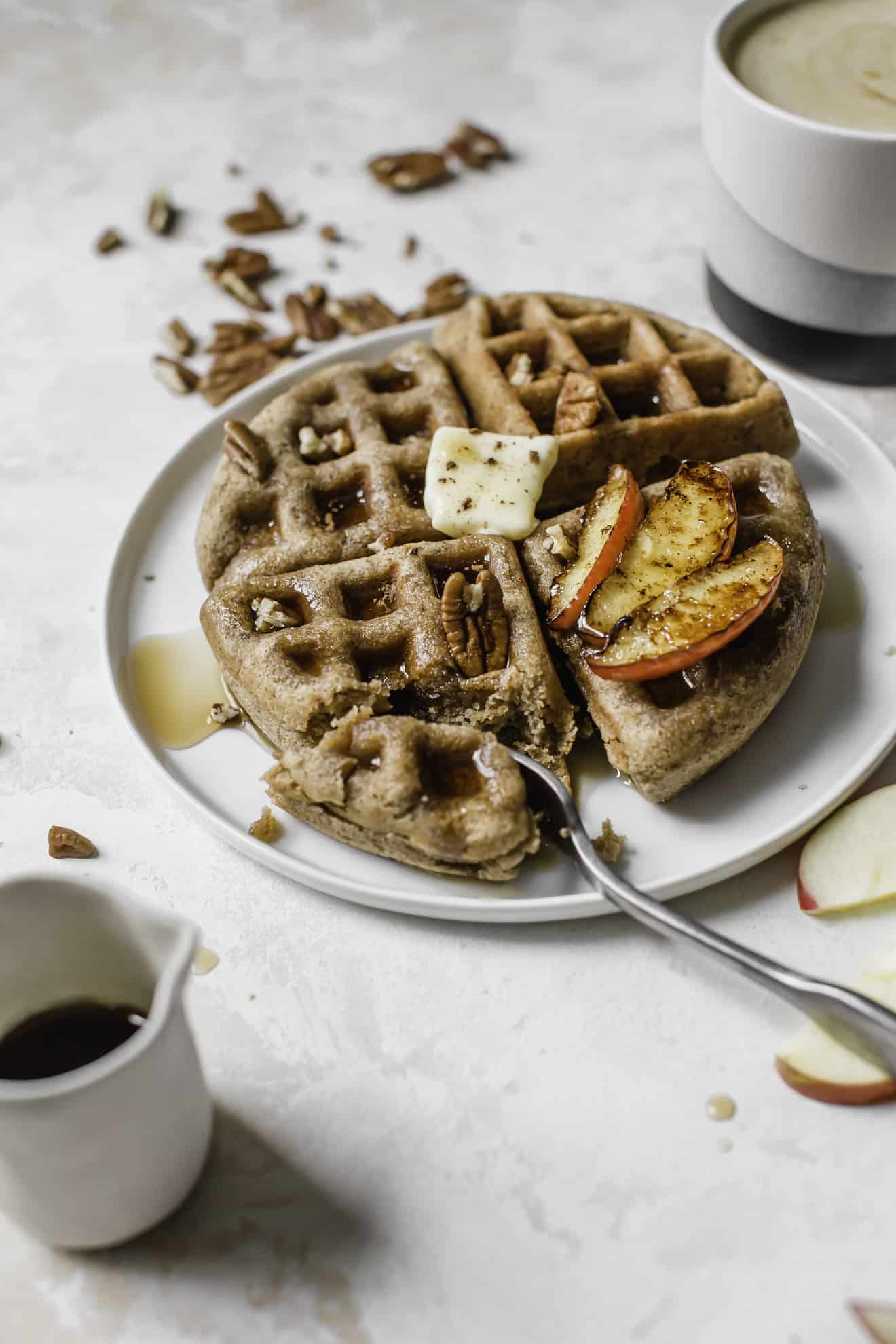 side angle of a pumpkin spice waffle with butter, maple syrup, pecans, and apples