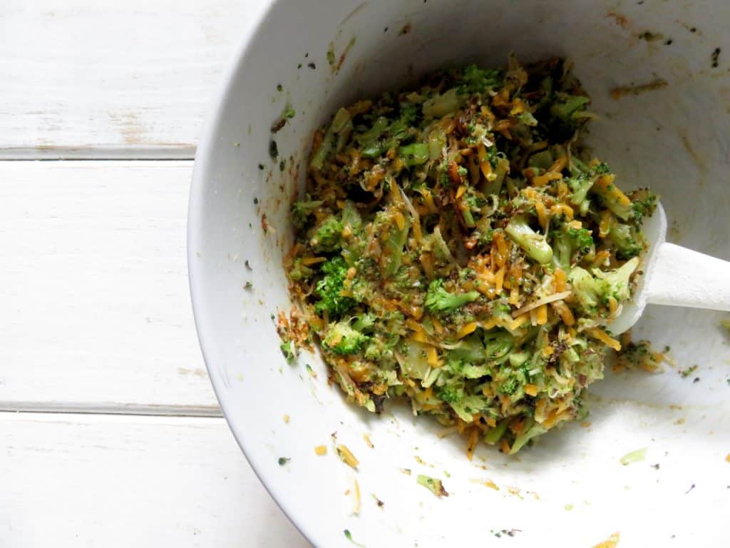 This is a white bowl with a broccoli cheese mixture in it. The bowl sits on white wooden planks.