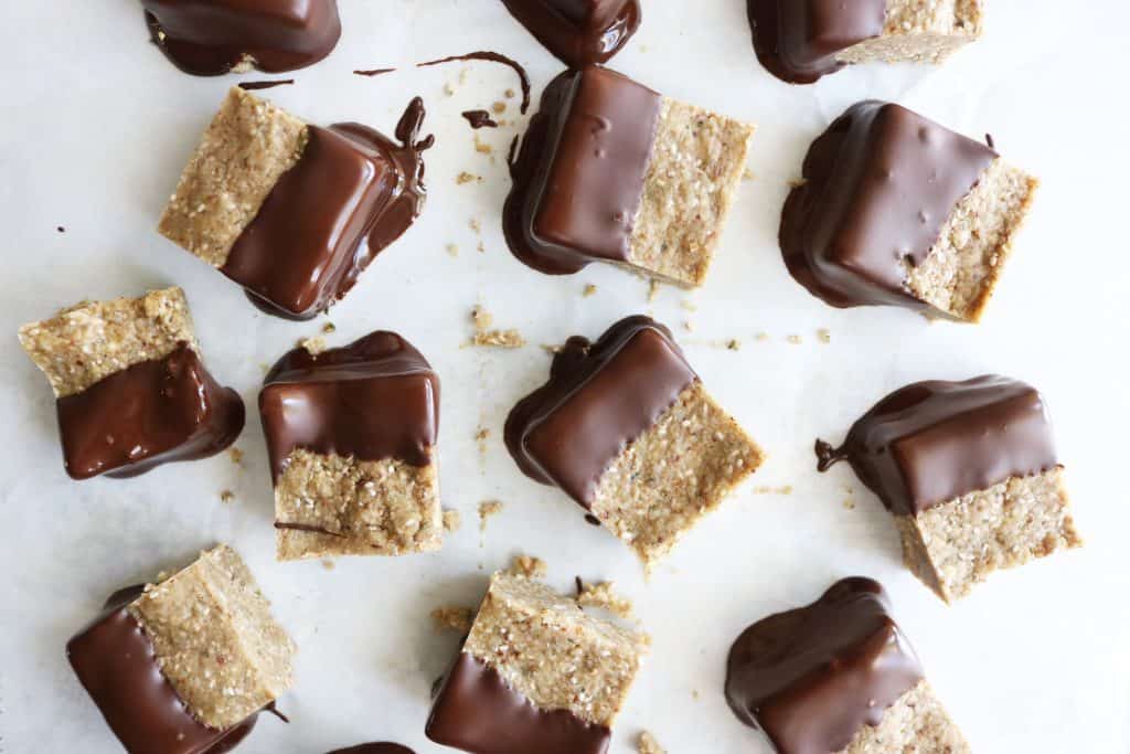This is an overhead image of small sunflower seed butter squares half dipped in chocolate. This image is included in a roundup of 50+ recipes for healthy snacks. 