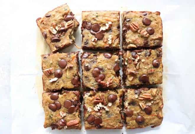 This is an overhead image of carrot zucchini squares. The bars are cut into 9 squares. The bars are topped with pecans and chocolate chips.