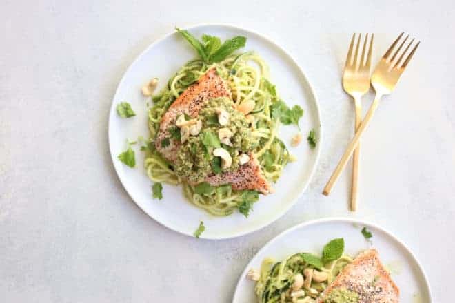 This is an overhead image of salmon on top of zoodles. On top of the salmon is a pesto and chopped nuts. 