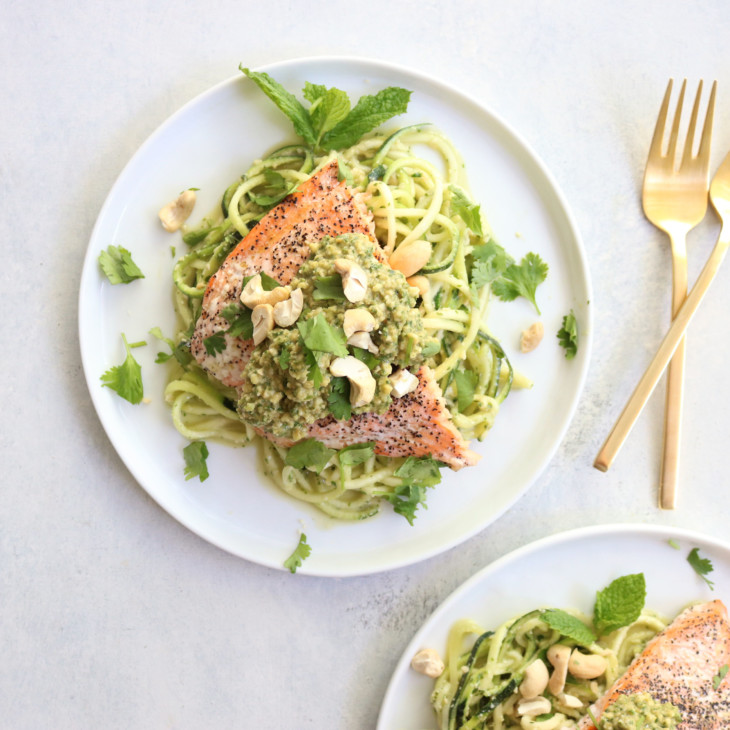 This is an overhead view of a plate with zoodles and salmon. The salmon has pesto and fresh herbs.