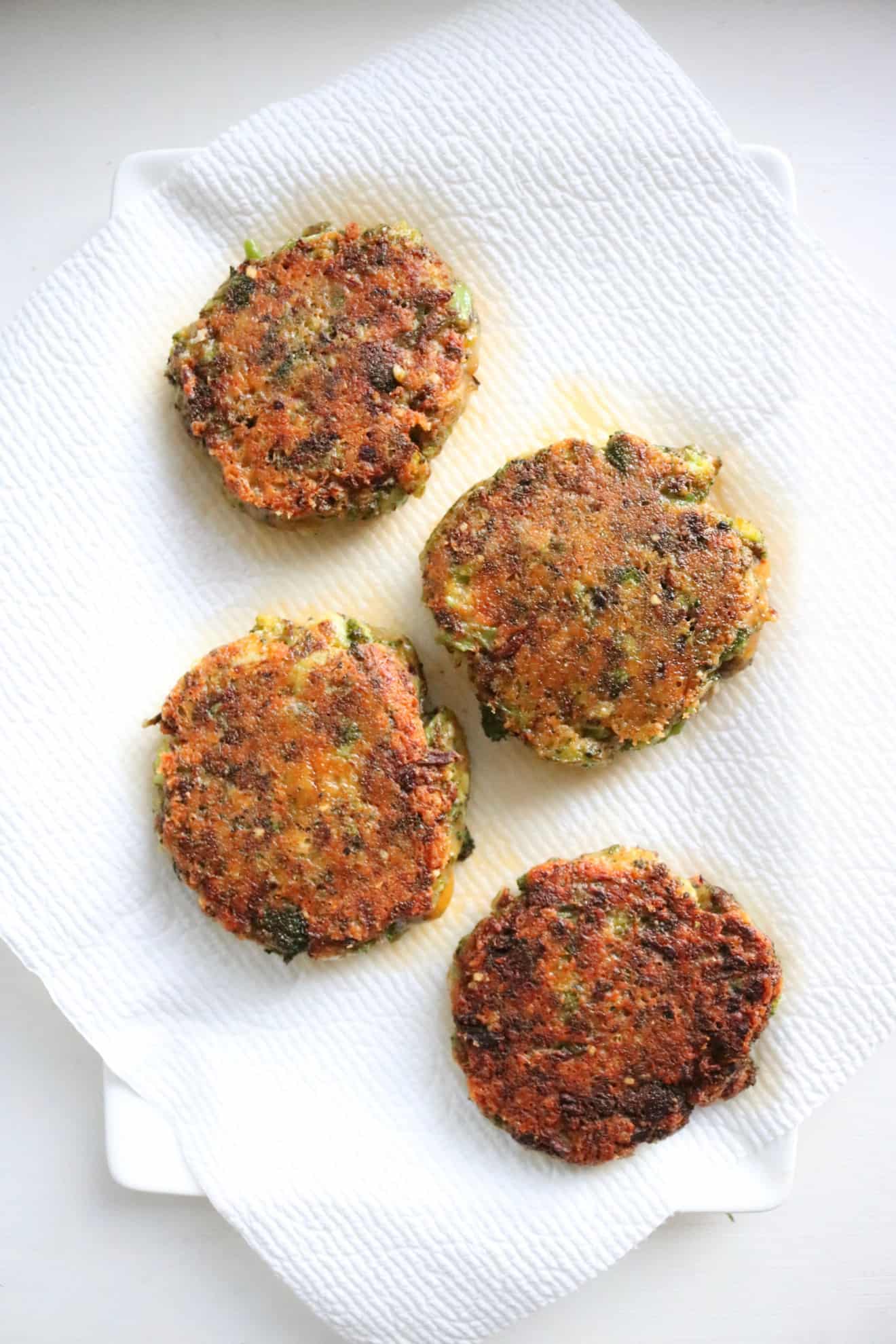This is an overhead image of four broccoli cheddar patties golden brown and fried on the outside The patties sit on a white paper towel. 