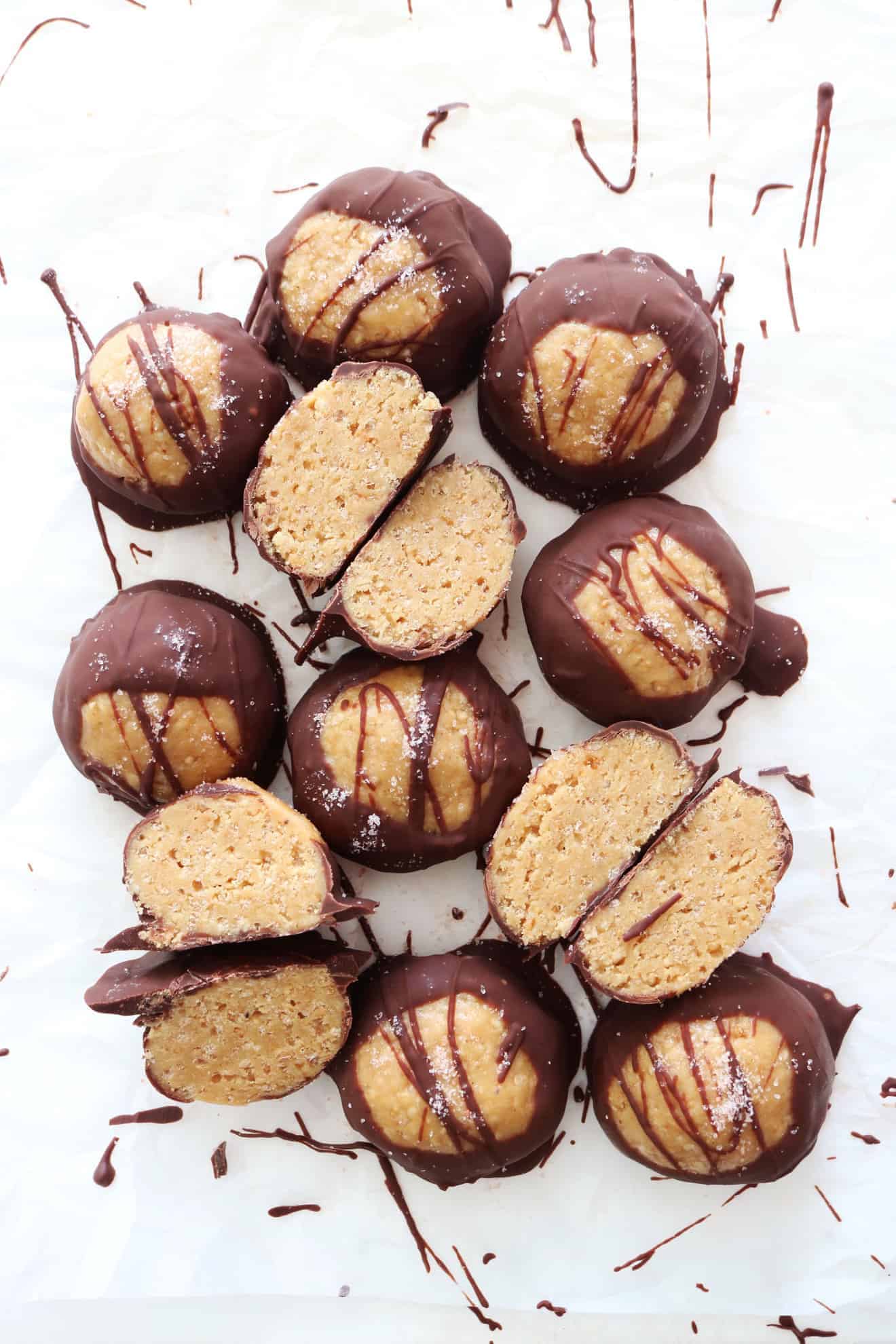 This is an overhead image of chocolate covered peanut butter balls. Some balls are sliced in half revealing a crunchy texture. The balls sit on a white background. 