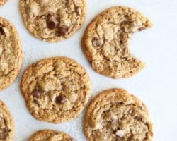 This is an overhead image of chocolate chip cookies laid out on a white surface. One cookie has a bite taken out.