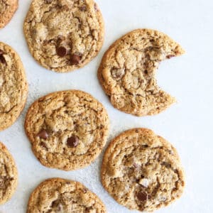 This is an overhead image of chocolate chip cookies laid out on a white surface. One cookie has a bite taken out.