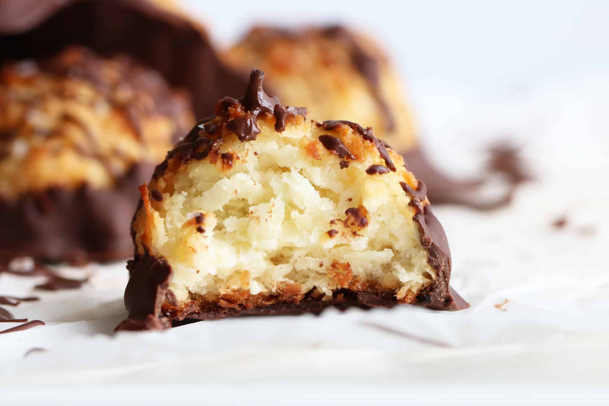 Side view of a coconut macaroon with harden chocolate and a bite taken out of it on a white counter 