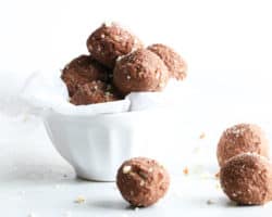 small white bowl filled with chocolate brazil nut energy balls with three energy balls sitting on the white counter