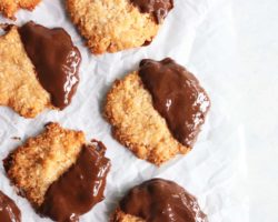 This is an overhead image of coconut cookies dipped half in melted chocolate. The cookies are on a white piece of parchment paper.