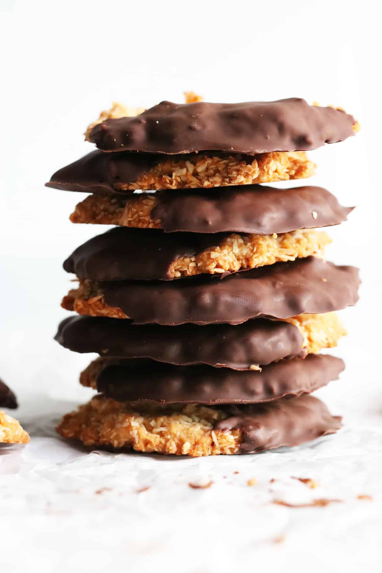 This is a stack of coconut cookies half dipped in chocolate. The stack of cookies is on a white surface with a white background. 