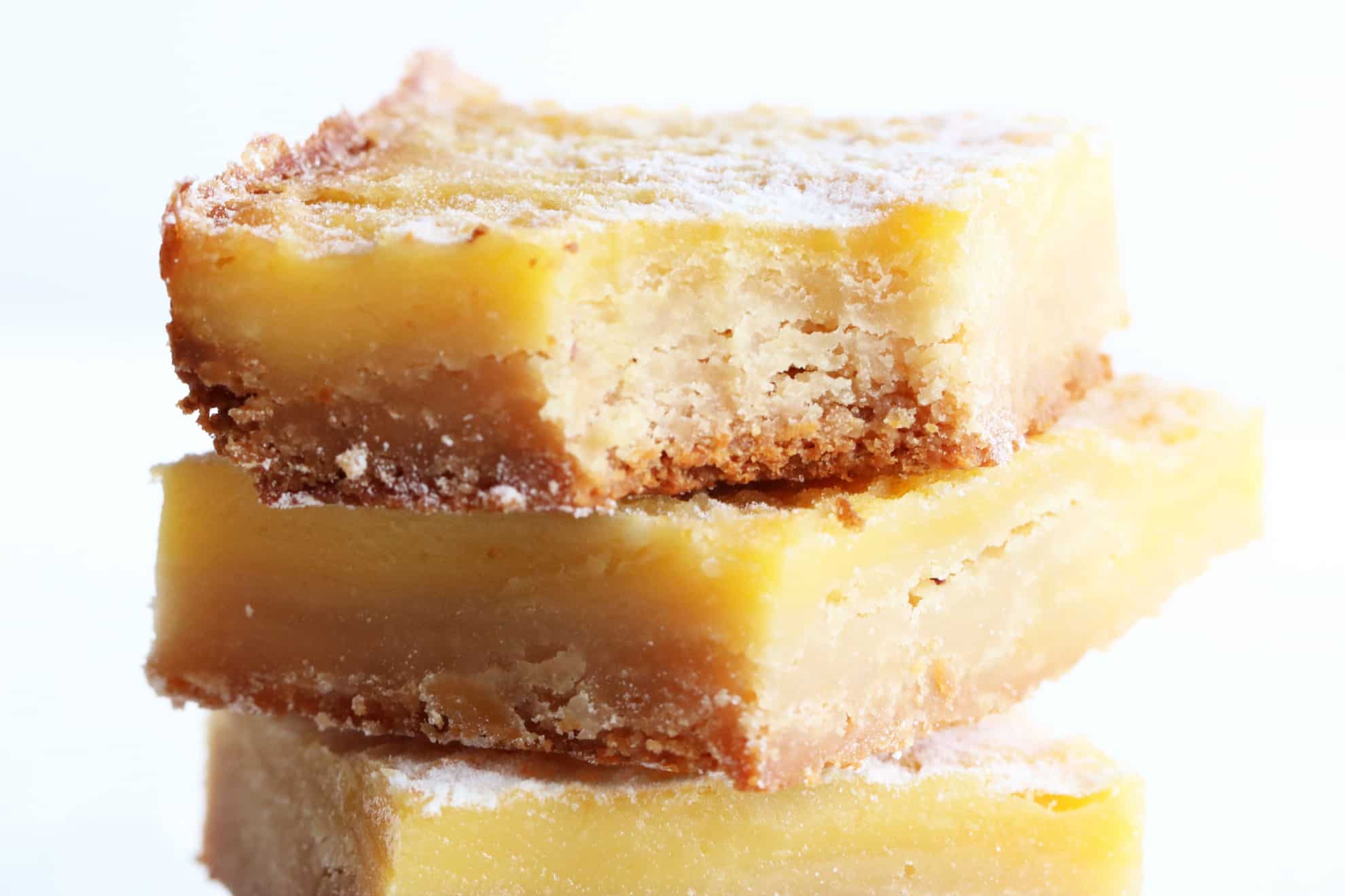This is a close up image of a stack of lemon bars. The top bar has a bite taken out of it. 