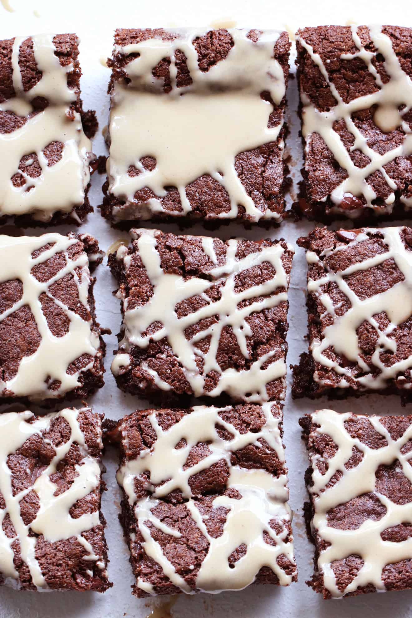 This is an overhead image of tahini brownies cut into squares. The brownies are drizzled with tahini in a criss-cross pattern.
