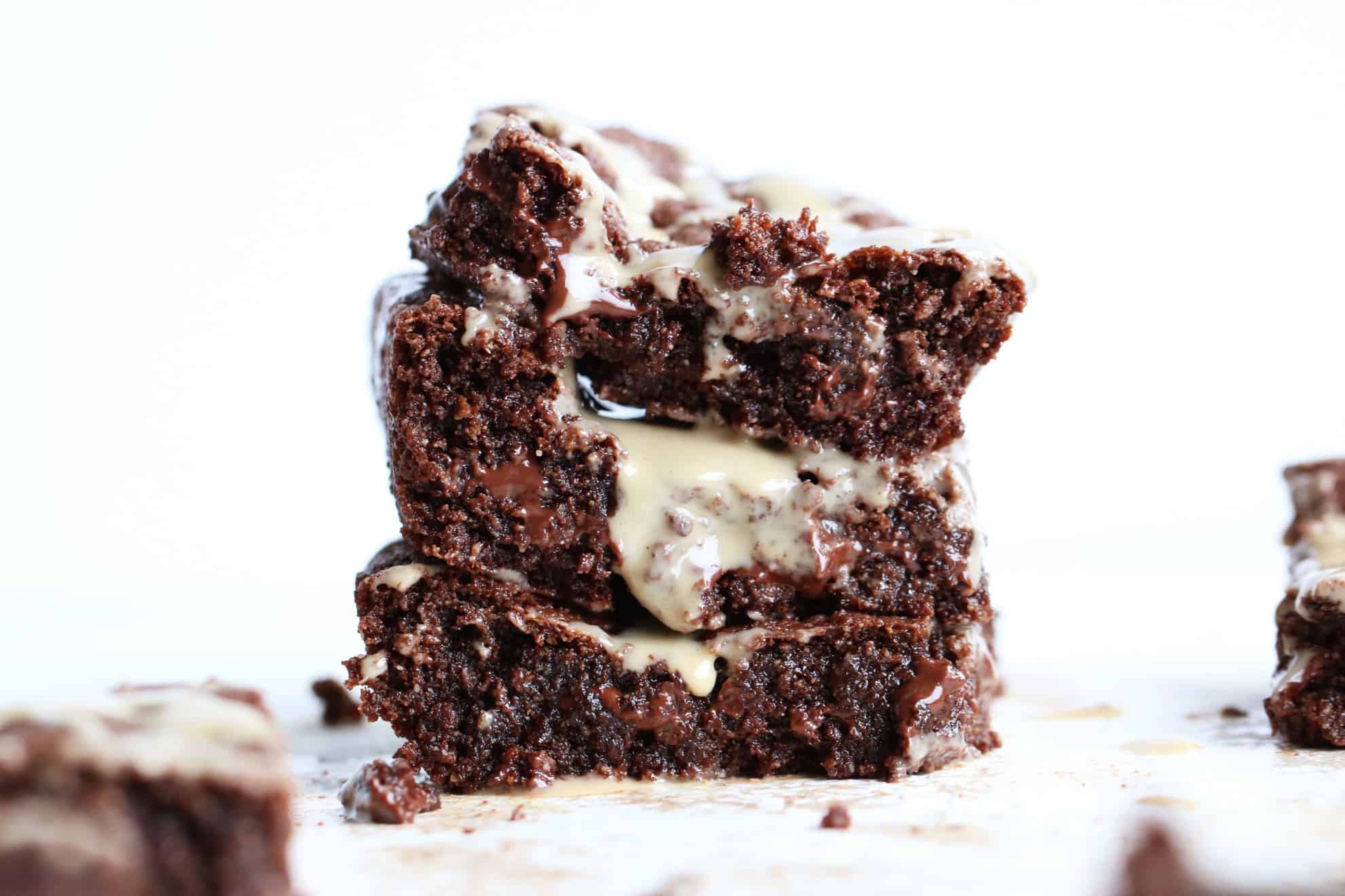 This is a side view of a stack of three tahini brownies. The stack sits on a white counter and is dripping with a drizzle of tahini.