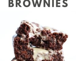 This is a side view of a stack of three tahini brownies. The stack sits on a white counter and is dripping with a drizzle of tahini. Text overlay reads "the best tahini brownies."