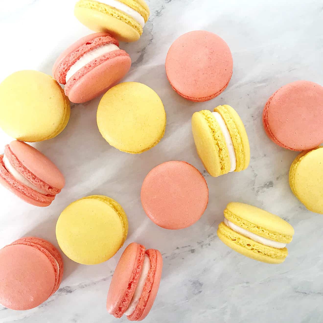 yellow and pink french macarons with vanilla icing filling on marble slab