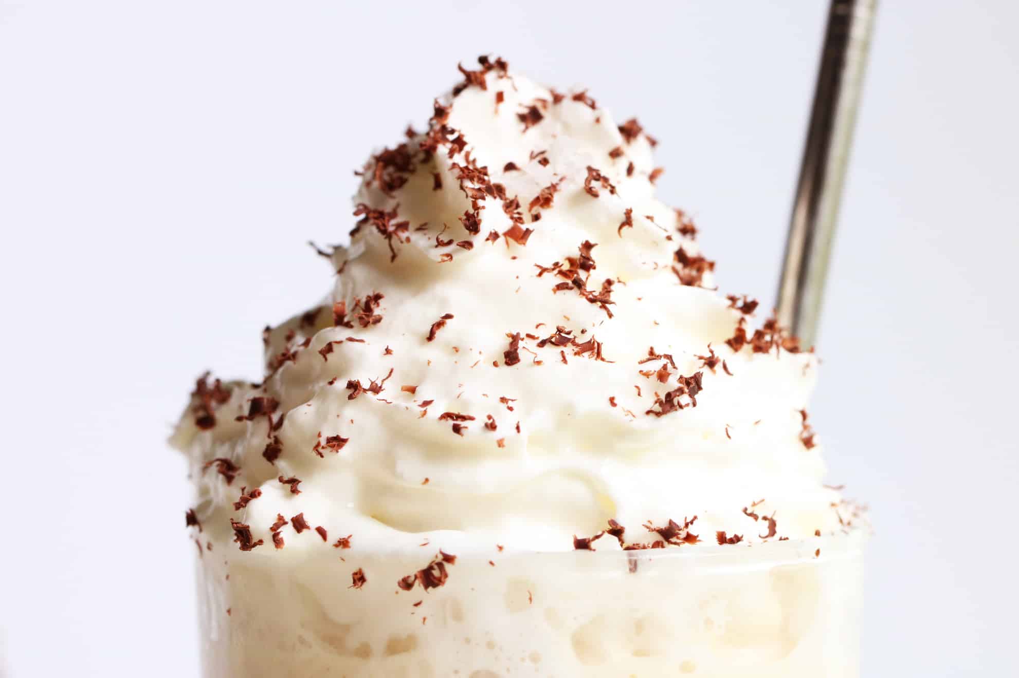 close up picture of whipped cream on top of a Frozen Vanilla Iced Latte with grated chocolate and a stainless steel straw