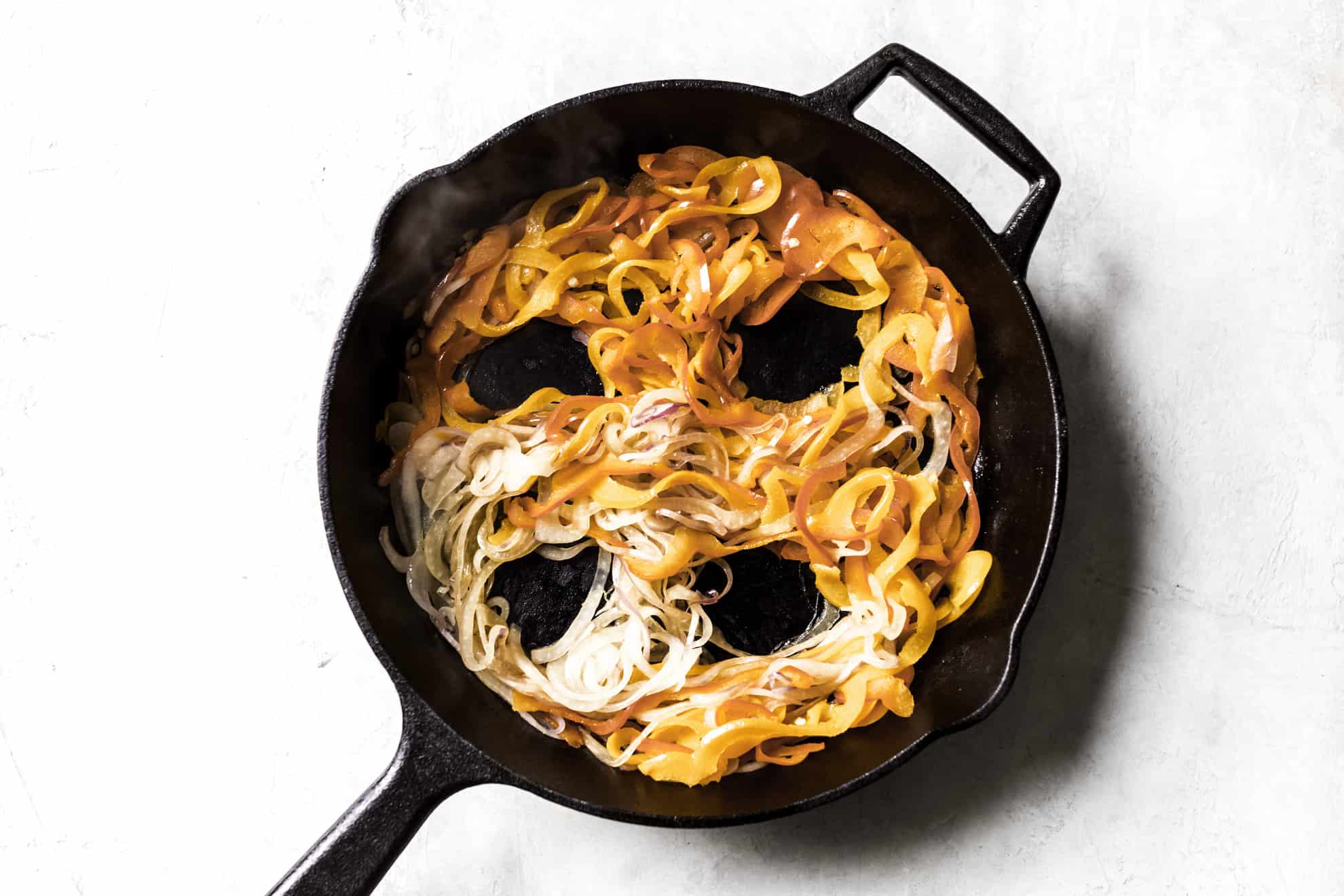 This is an overhead image of a cast iron skillet on a white surface. Inside the skillet is cooked peppers and onions with four divots for eggs to eb cracked in. 