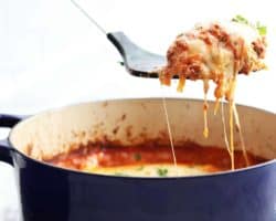 side view of a spatula pulling up a cheesy slice of butternut squash lasagna out of the blue dutch oven