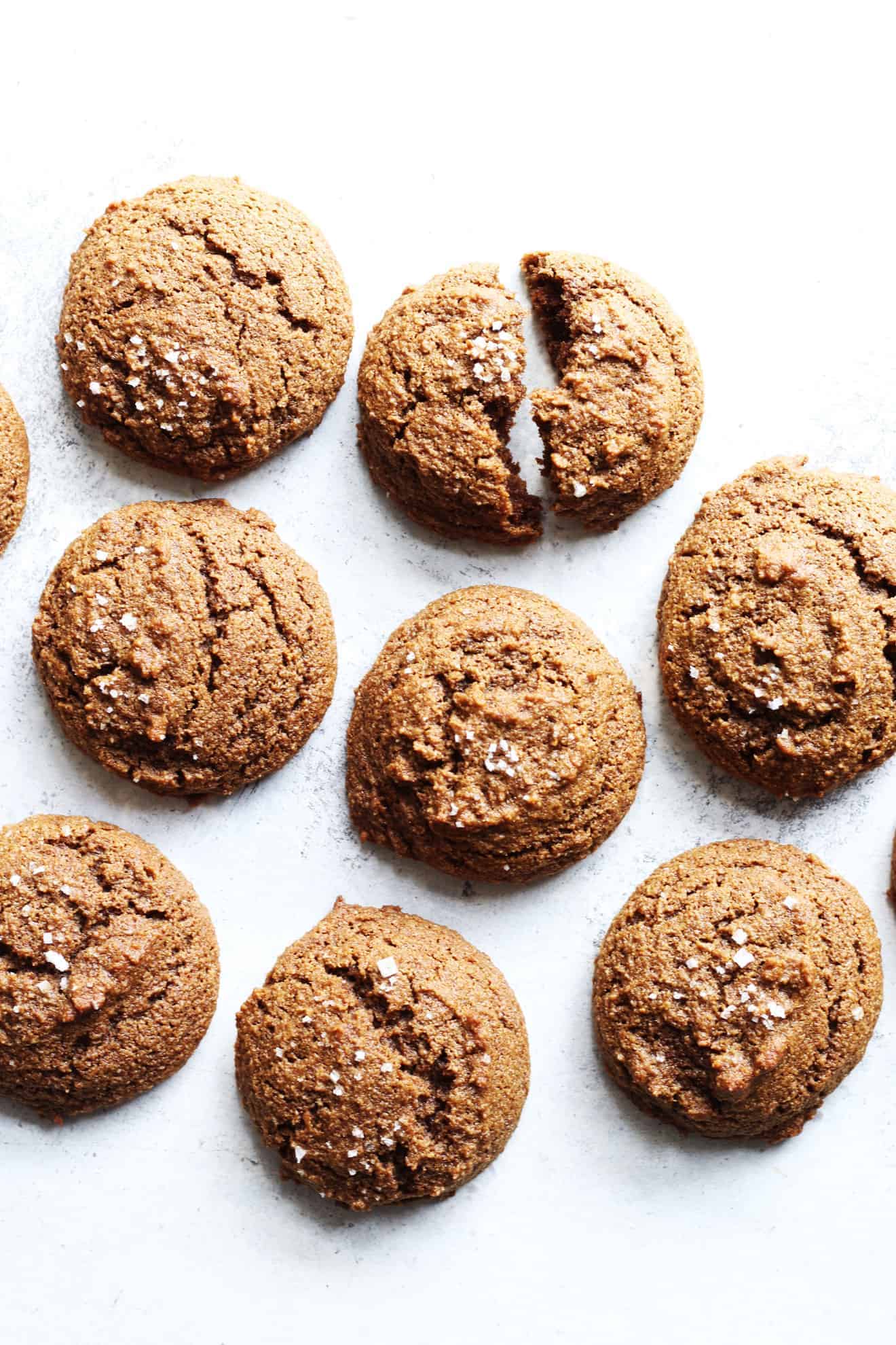 overhead image of a group of Soft Baked Ginger Molasses Cookies on a white counter, one is broken in half and laying in the group of cookies