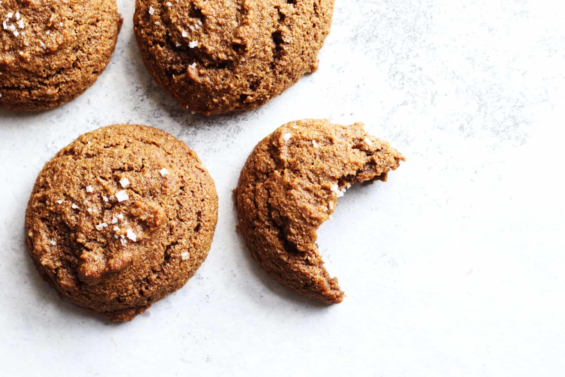 overhead image of Soft Baked Ginger Molasses Cookies on white counter, one has a bite taken out