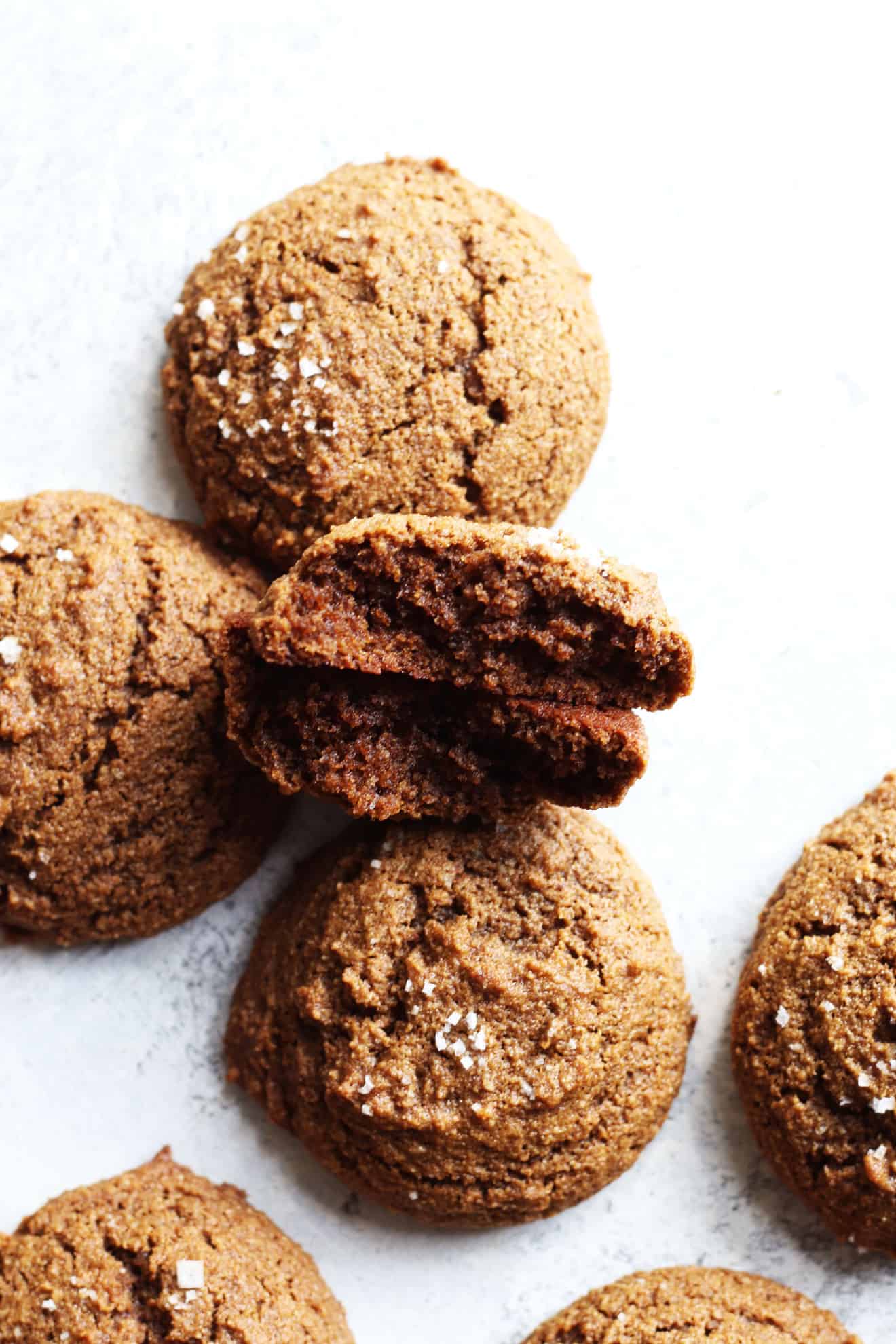 overhead image of soft ginger cookies on a white counter, one cookie is broke in half and layered on top of itself so you can see the inside. The broke cookie lays against other ginger molasses cookies.
