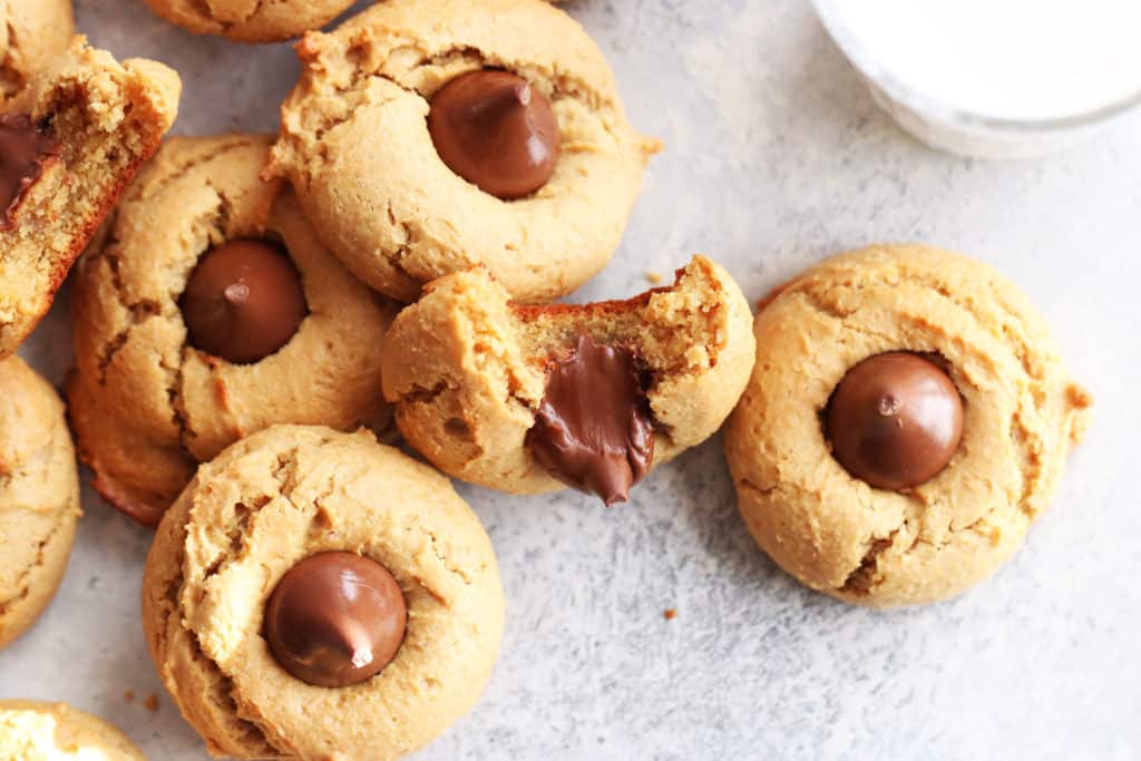 This is an overhead image of gluten free peanut butter blossom cookies. One cookie has a bite taken out and leaning against another. The cookies sit on a white and grey surface.