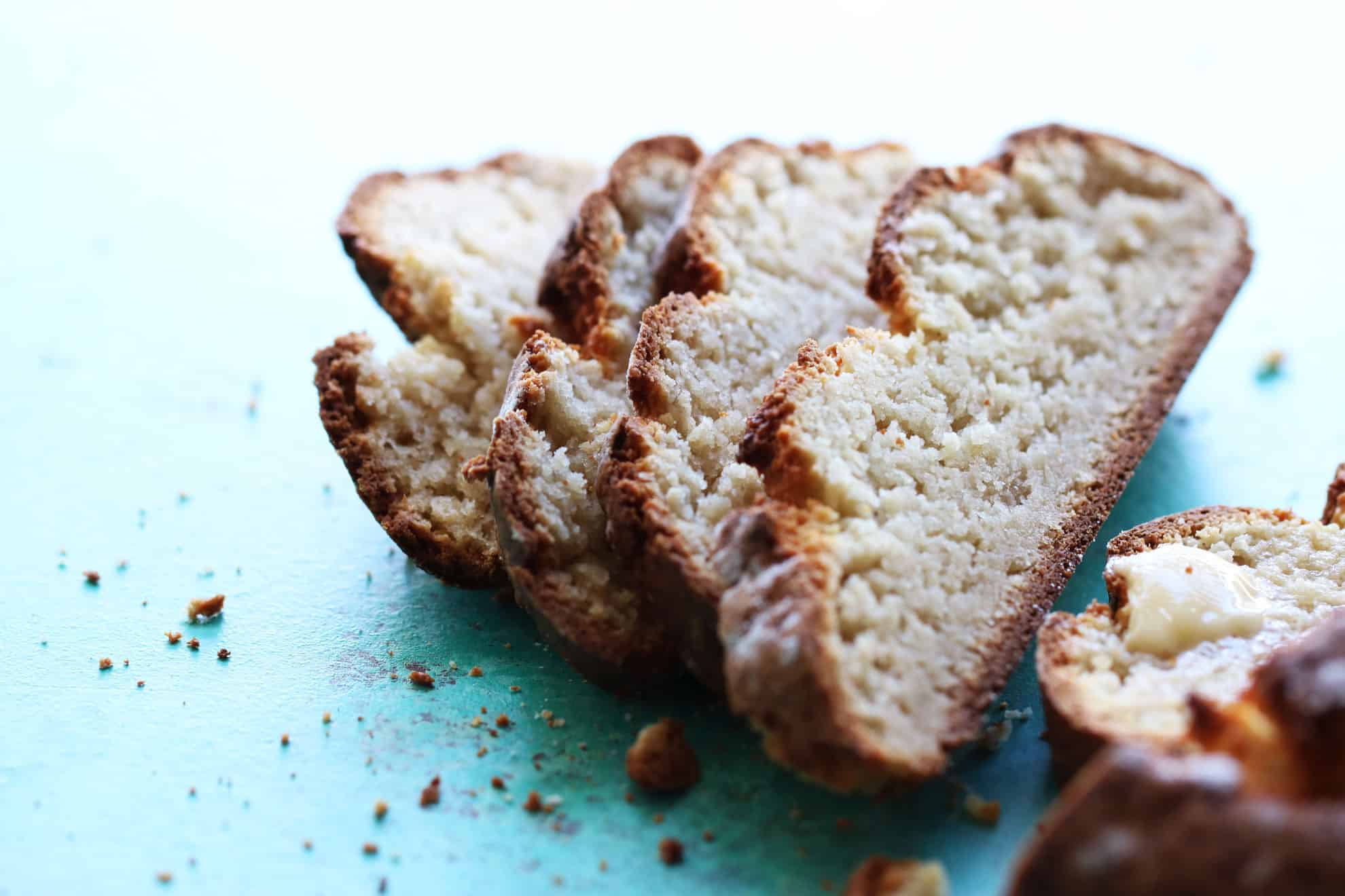 This is a side view of soda bread sliced and leaning against each other. The bread lays on a turquoise surface with crumbs around it.
