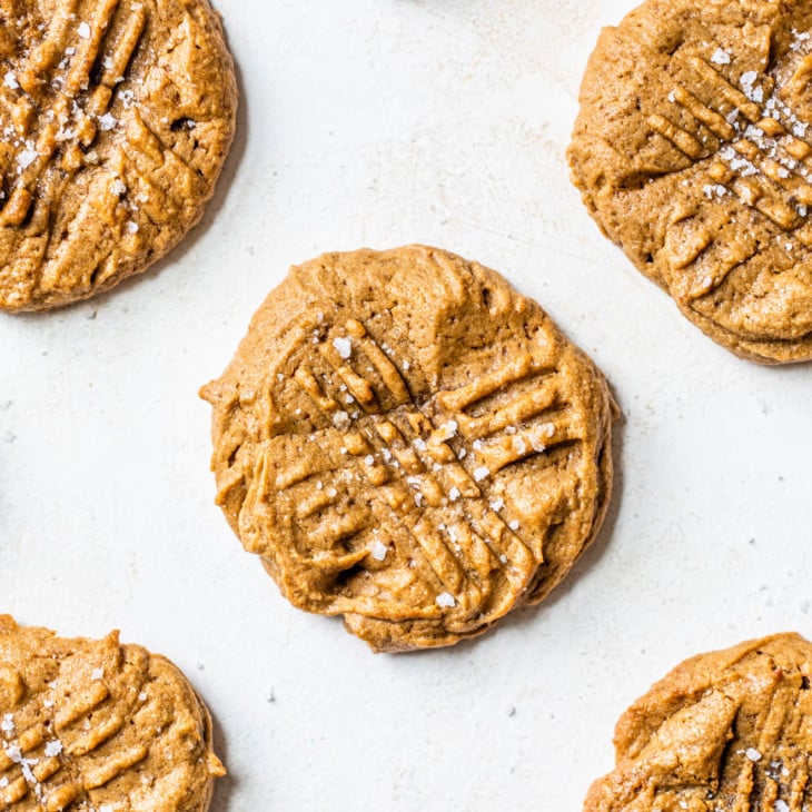 This is an overhead image of peanut butter cookies on a white background. The cookies have fork imprints and are sprinkled with salt on top.