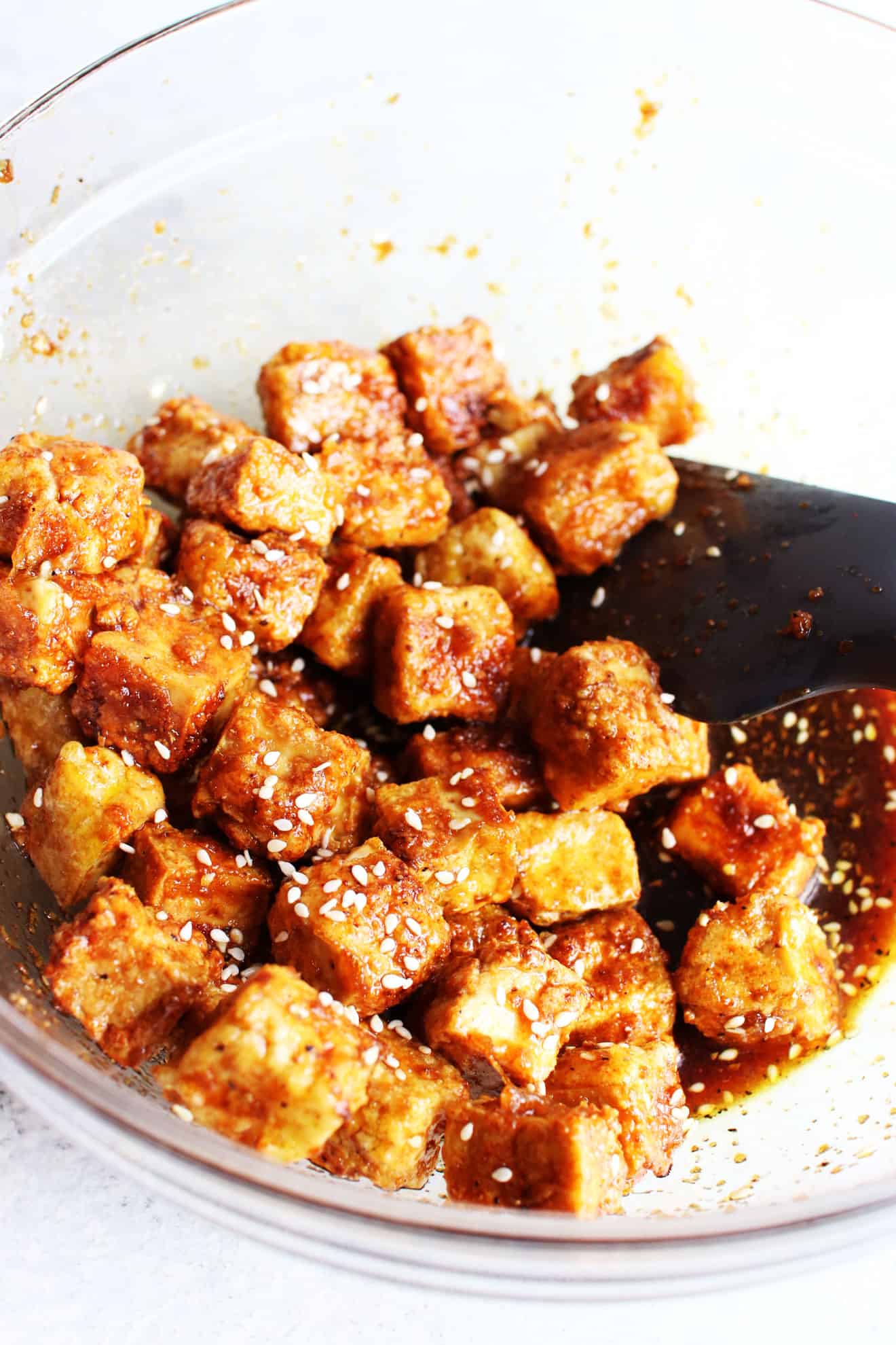 clear bowl filled with crispy cubes of tofu, a soy marinade sauce and sesame seeds.
