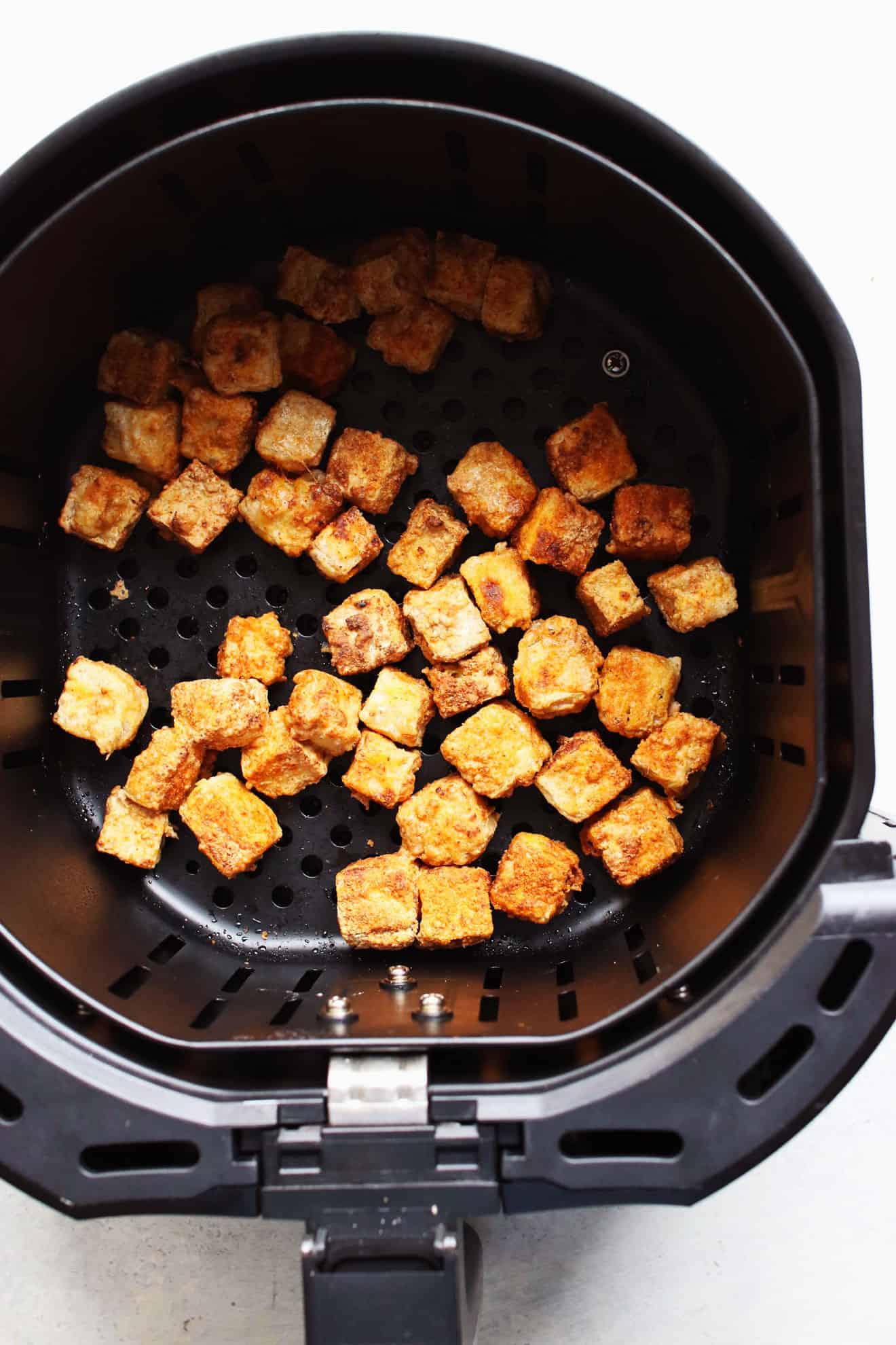 air fryer basket with crispy cubes of tofu inside.