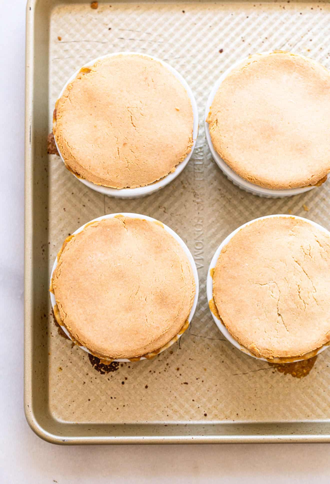 This is an overhead image of chicken pot pie in four small ramekins. The ramekins sit on a gold baking sheet which is on a white counter. 