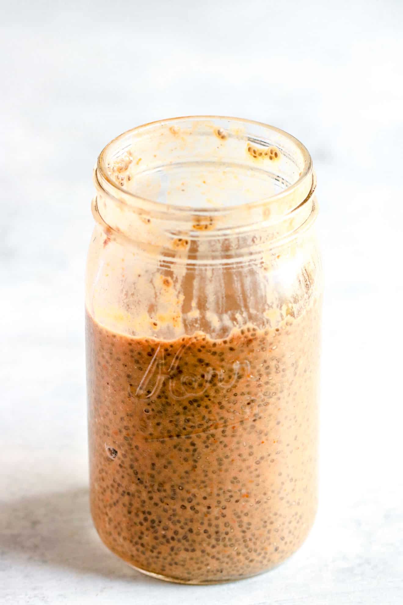 mason jar filled with chia seeds, milk, pumpkin, and other ingredients mixed up on grey counter