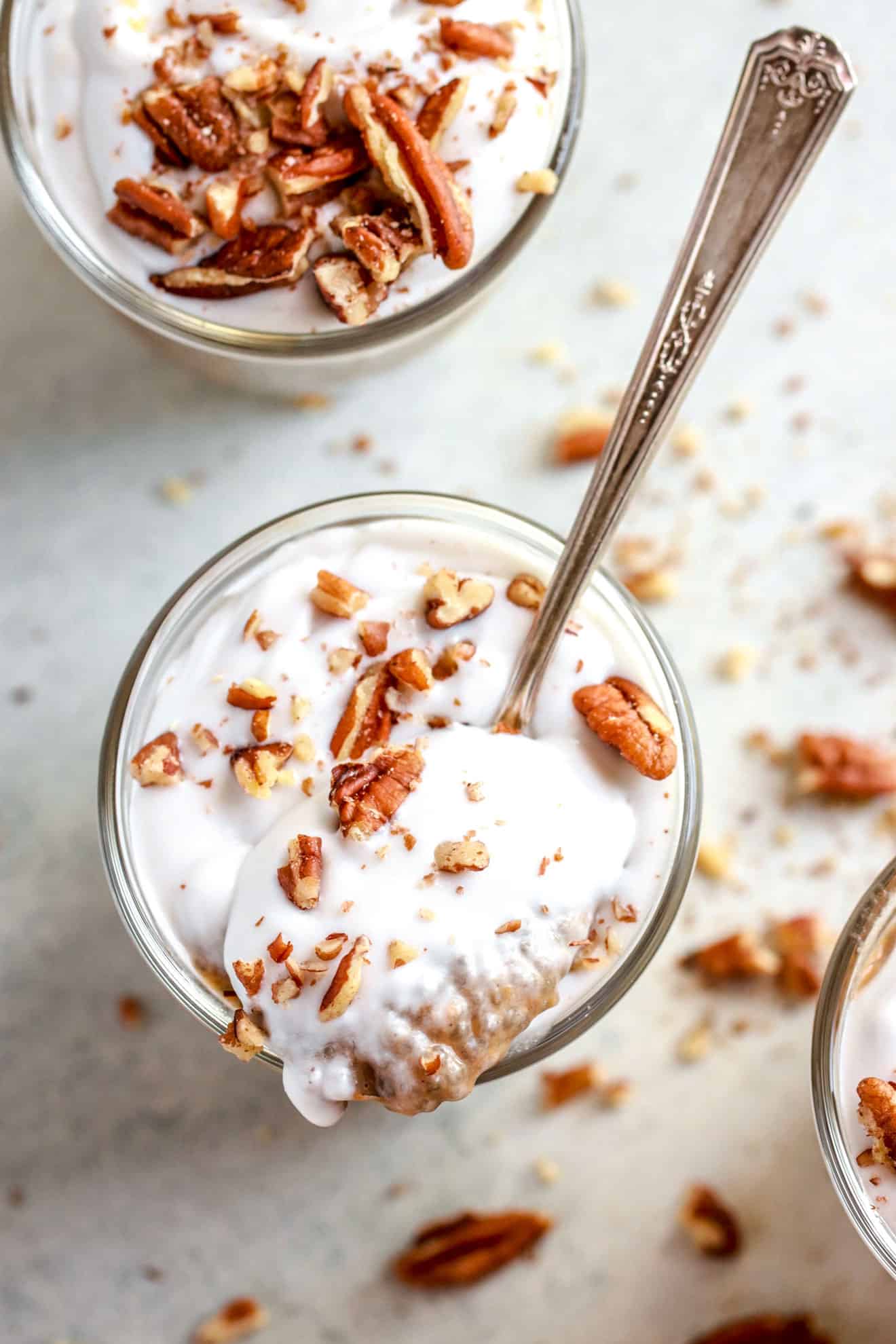 Overhead image of vegan pumpkin chia pudding with a spoon scooping some, topped with coconut cream and chopped pecans