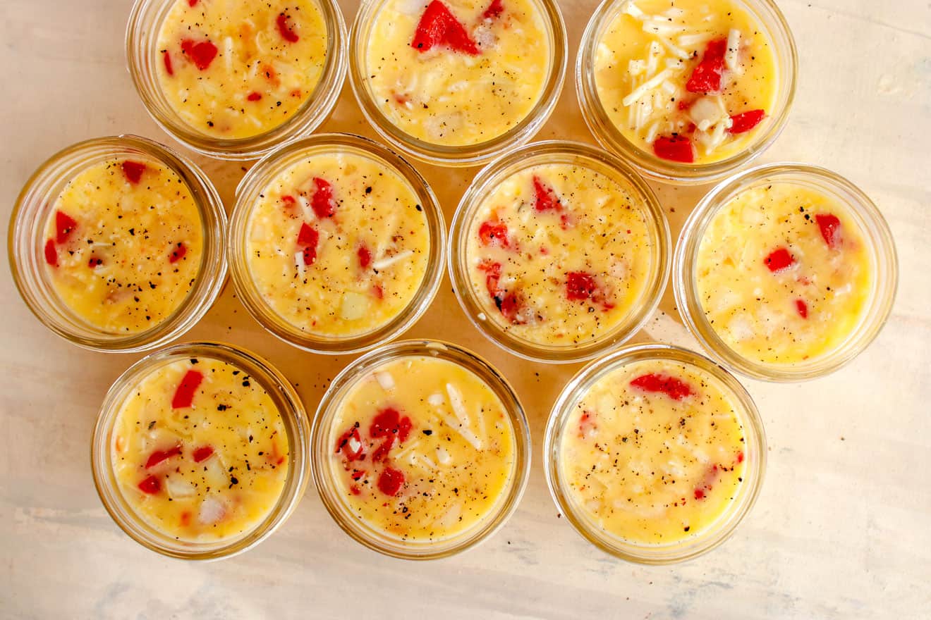 This is an overhead image of small glass jars filled with eggs, peppers, and cheese. The egg mixture is topped with ground epper.