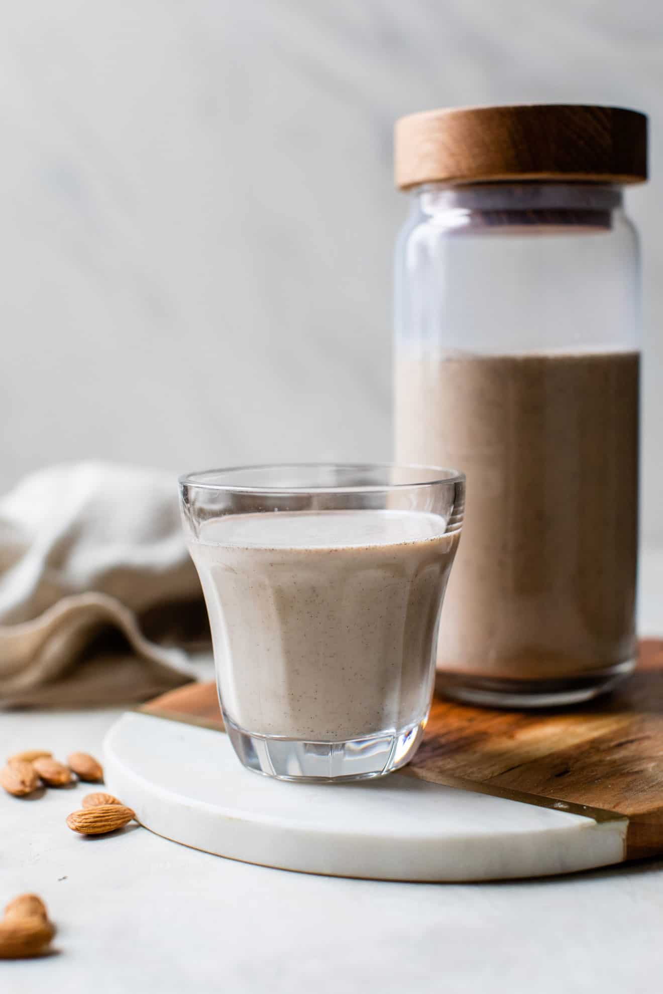 vanilla almond milk in a glass with a pitcher of almond milk behind it, almonds on the table, white background