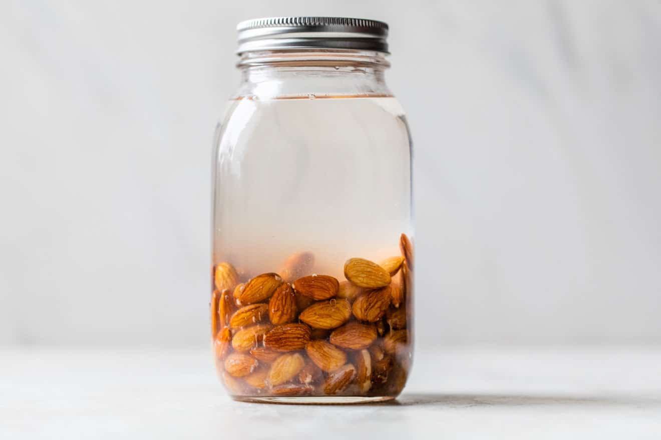 almonds soaking in water in a glass macon jar with a lid, white, marble background