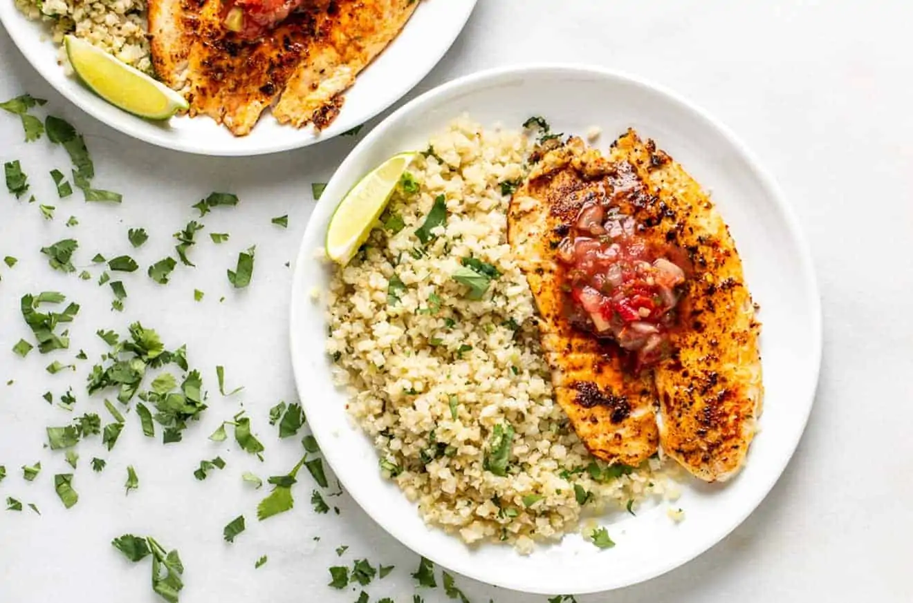 blacked tilapia with salsa on top and cauliflower rice on a white plate on marble with cilantro