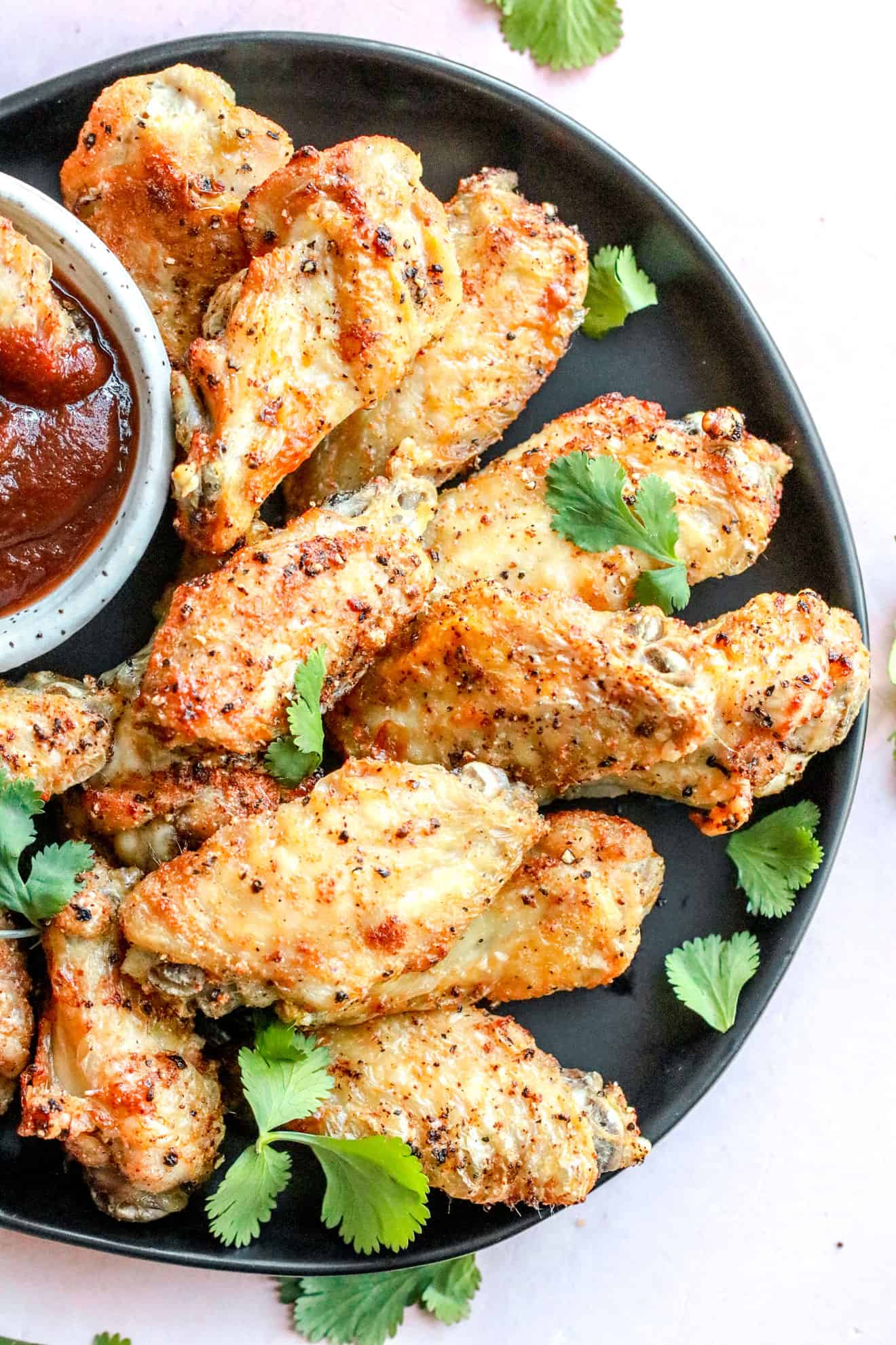 crispy air fryer chicken wings on black plate with small bowl of bbq sauce on pink background