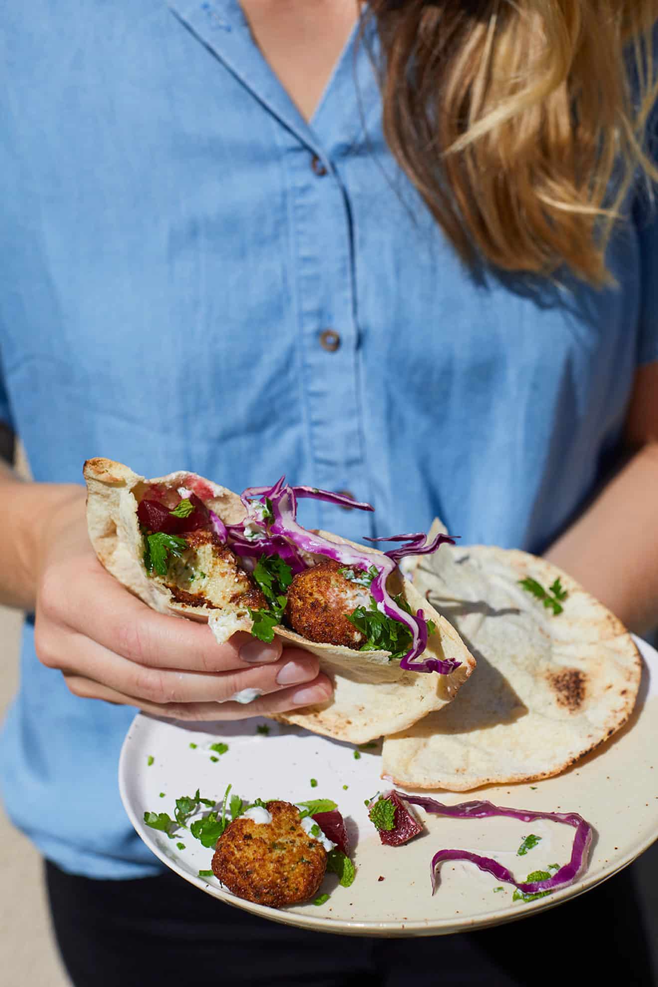 woman in blue shirt holding a pita filled with cauliflower falafel with cabbage, fresh herbs and tzatziki