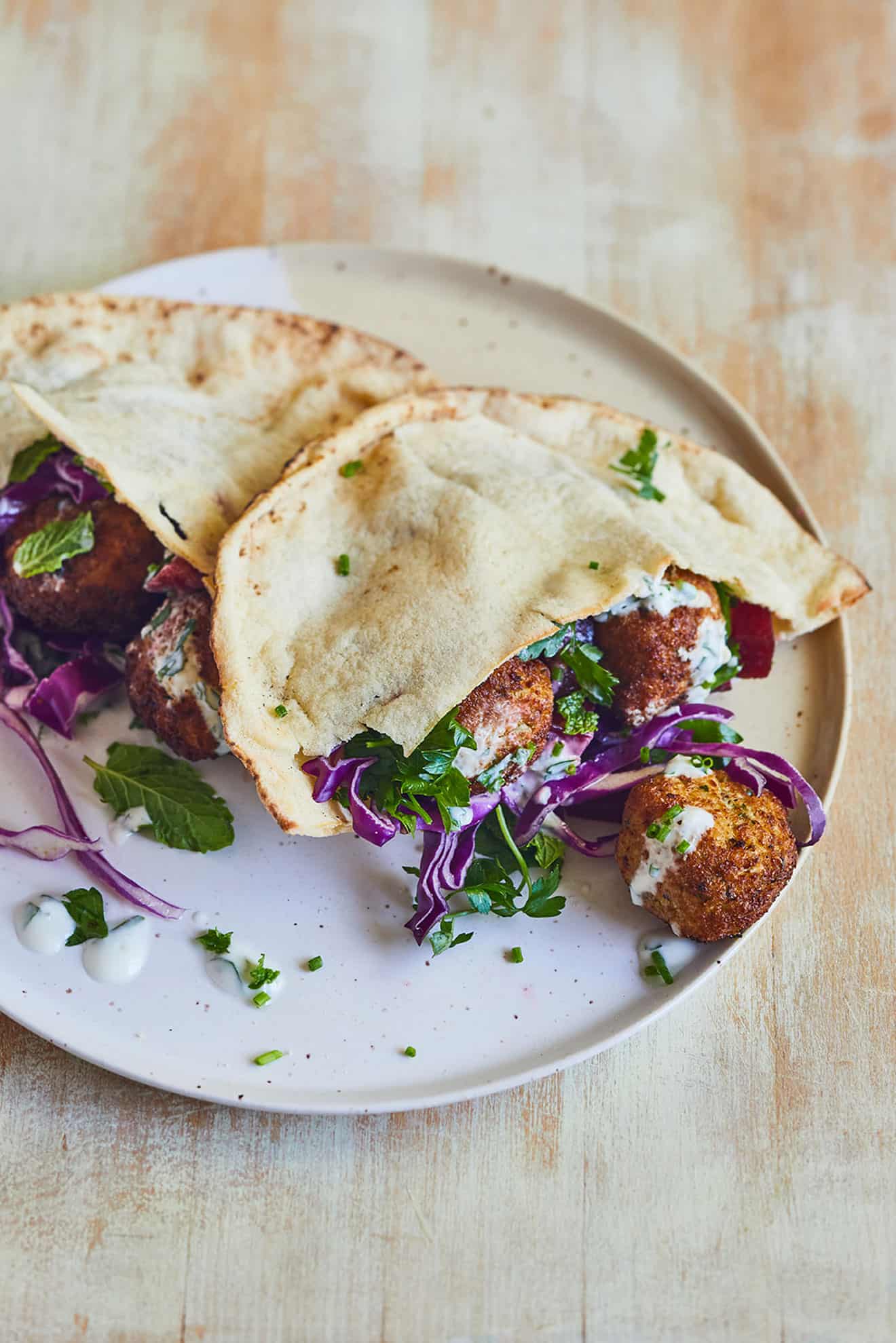 cauliflower falafel with cabbage, herbs and tzatziki in pita on white plate on cutting board