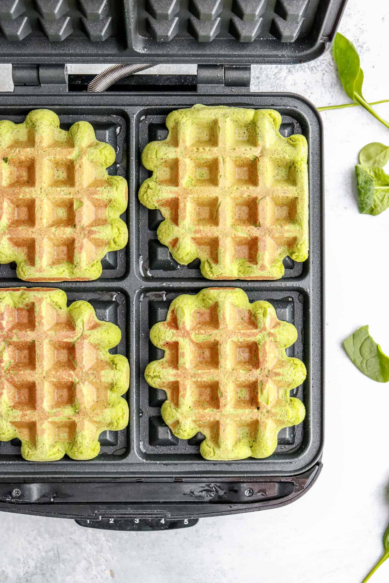 four green spinach waffles on a waffle iron
