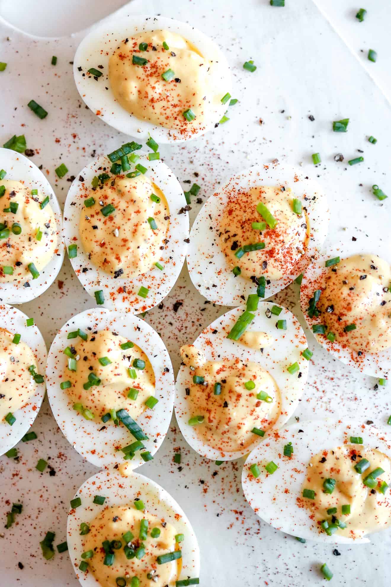 tray of deviled eggs with smoked paprika sprinkled on top and fresh chives on white background