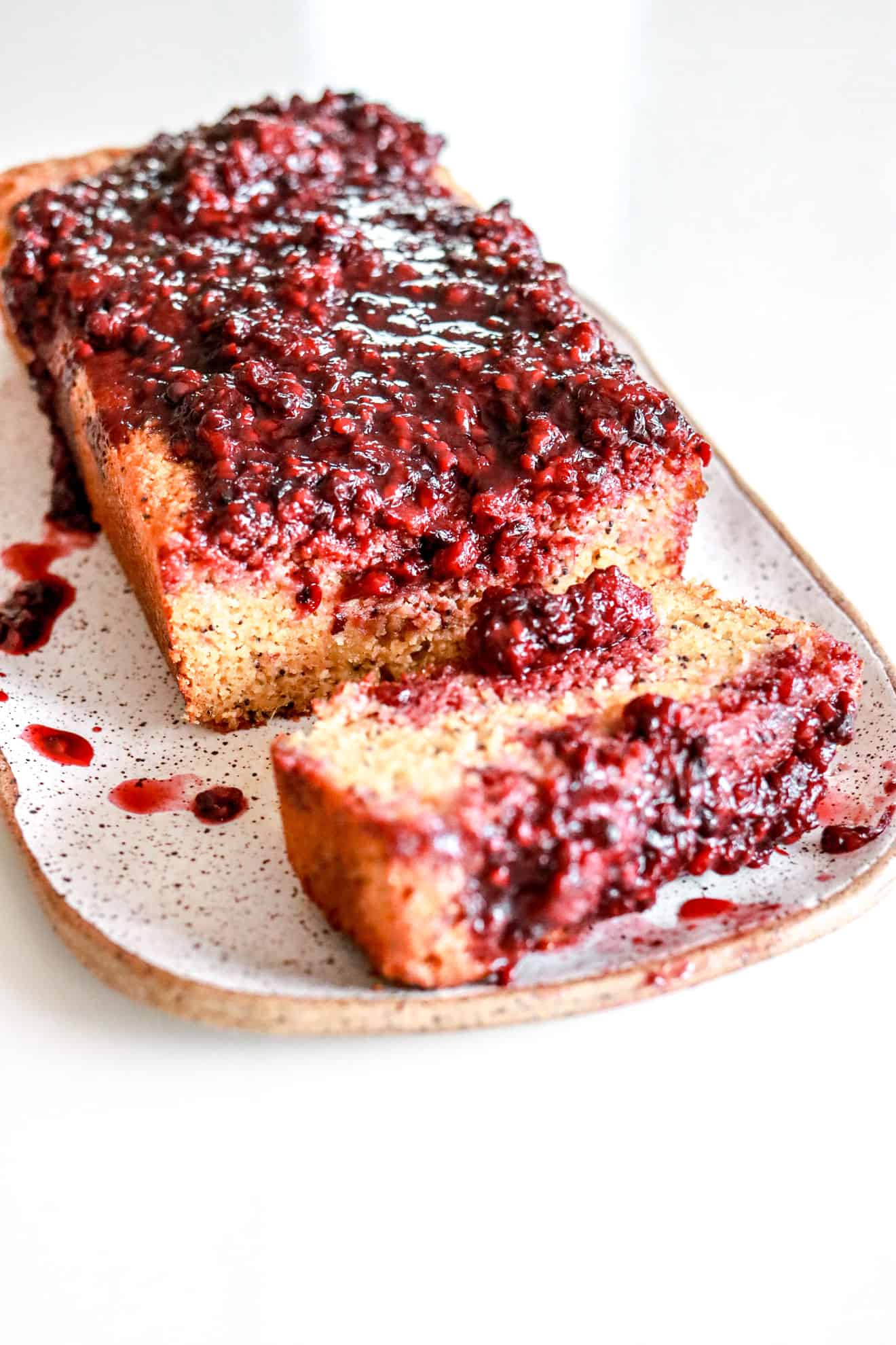 lemon poppy seed bread with blackberry glaze on top on a plate on a white counter