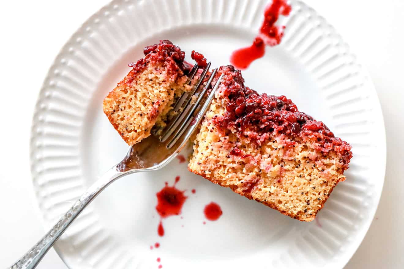 slice of lemon poppy seed bread with blackberry glaze on a white plate on white counter
