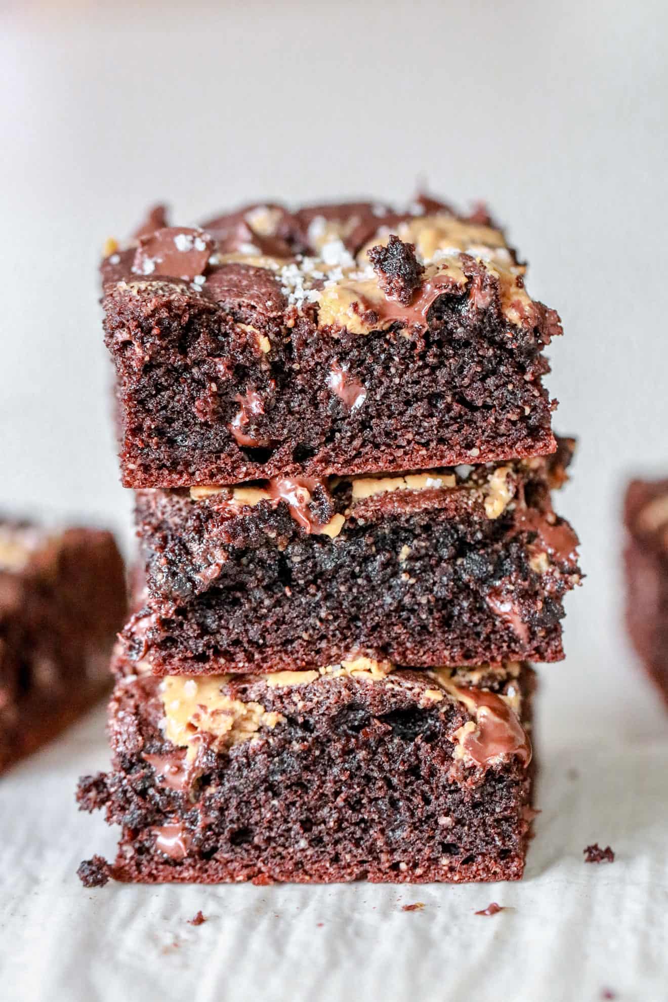 stack of three chocolate peanut butter swirl brownies on white parchment paper and white background