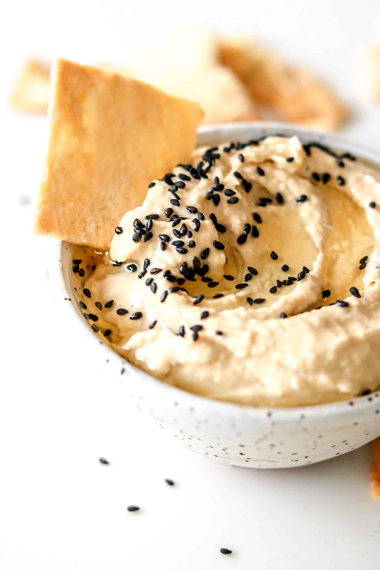 bowl of Sesame Tahini Hummus in a white speckled bowl with black sesame seeds on top and a pita chip