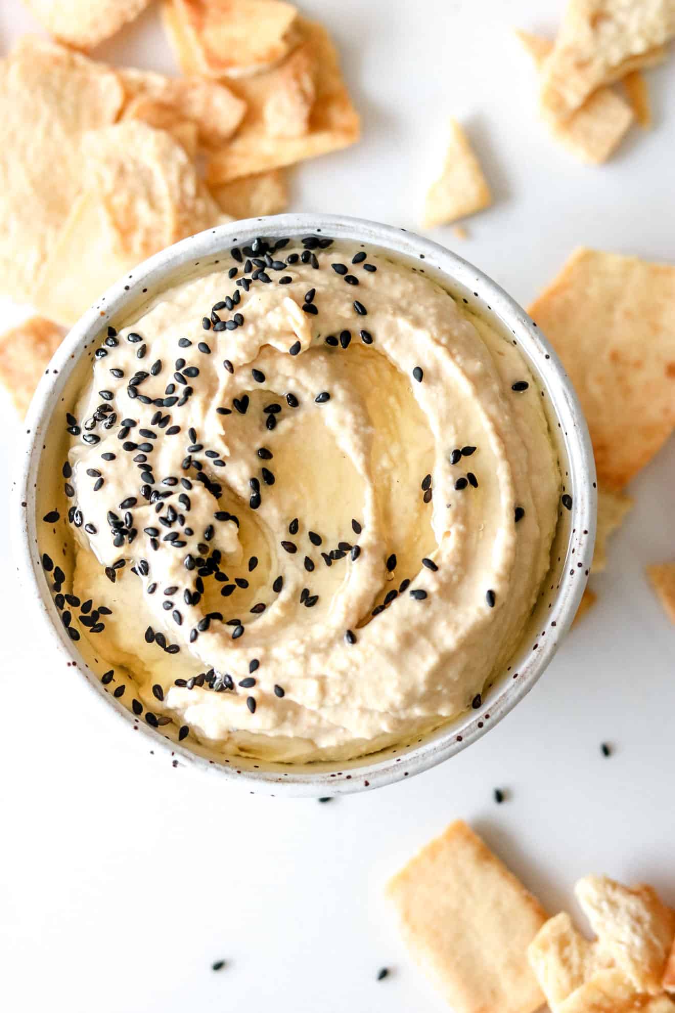 Sesame Tahini Hummus in white speckled bowl on white counter with pita chips