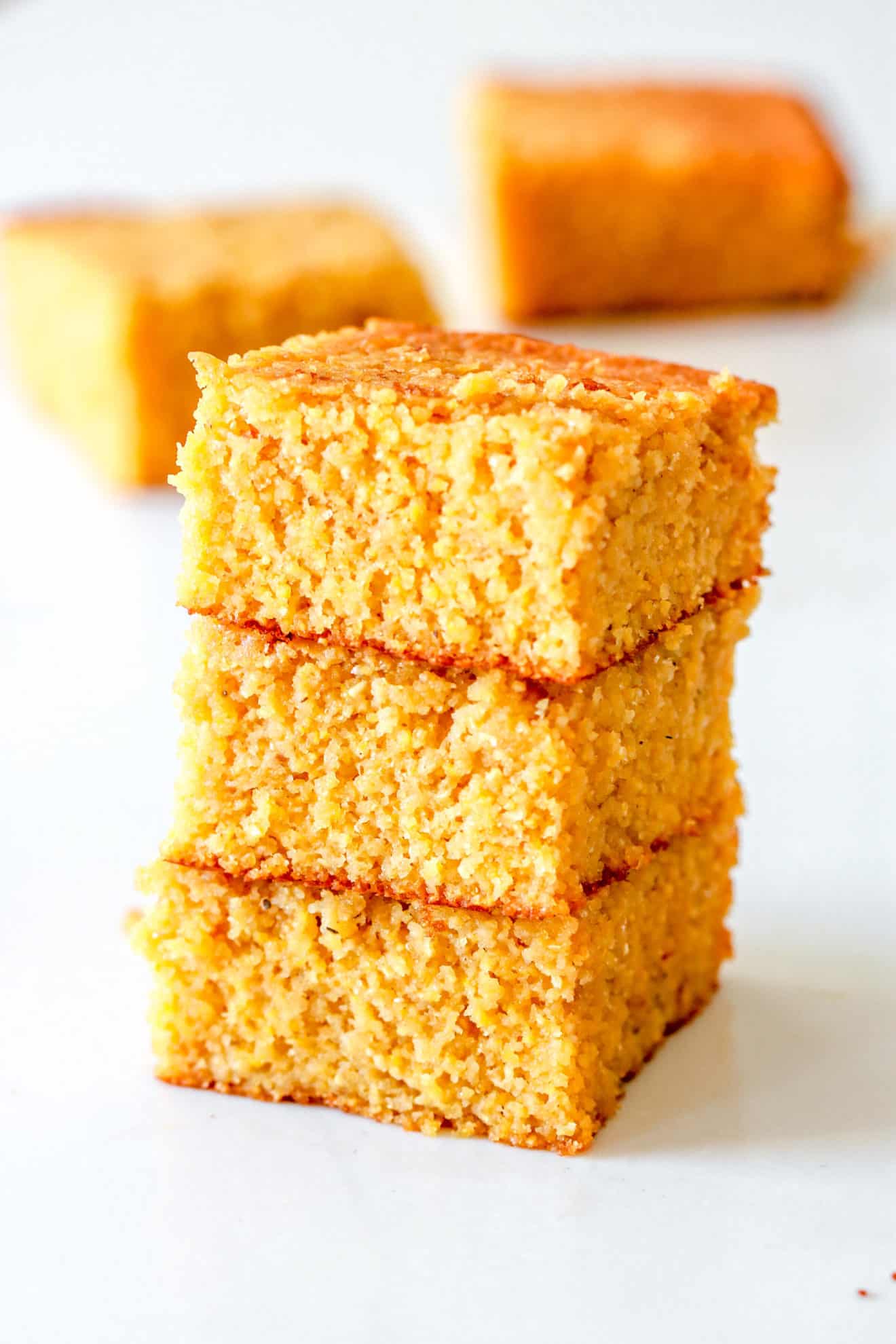 stack of buttermilk cornbread squares with more cornbread in the background on a white counter
