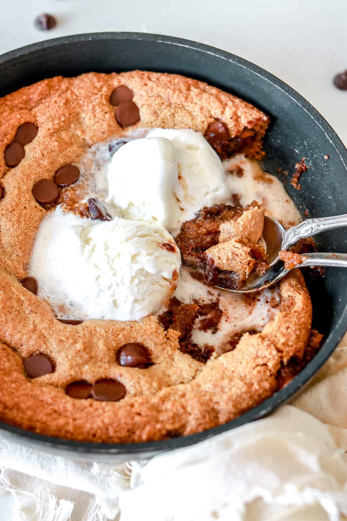 chocolate chip cookie skillet with melted vanilla ice cream on top and spoons
